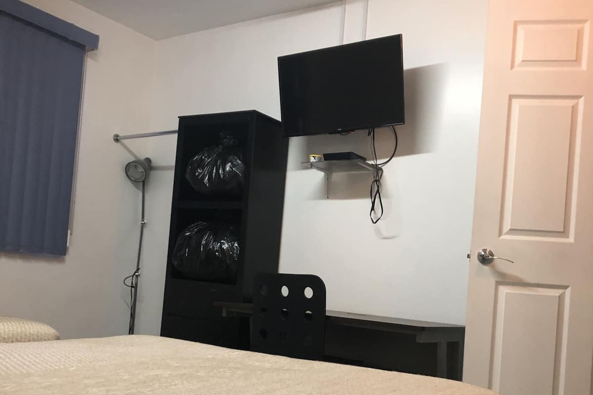 A bedroom with a bed, a desk, a chair, a TV mounted on the wall, and a door.