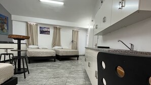 Ett kompakt hotellrum med två sängar, ett litet pentry och en matplats med barstolar.