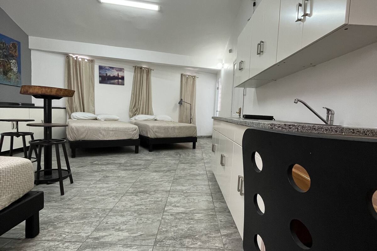 A compact hotel room with two beds, a small kitchenette, and a dining area with stools.