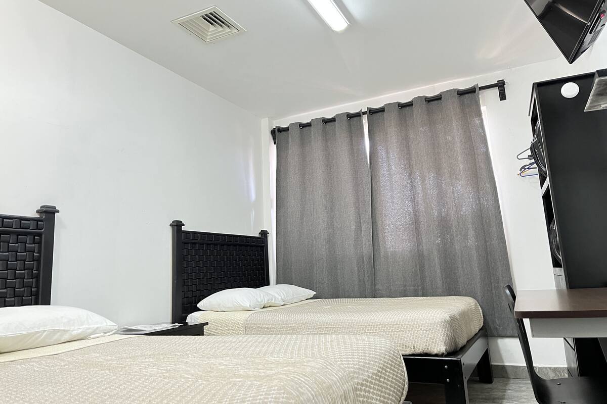 A hotel room with two beds, a desk, a television, and a window with curtains.