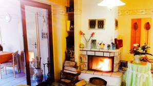A cozy living room with a fireplace, a dining area with a table and chairs, and a small side table with a vase. - Pension Fischerhaus (Trassenheide)
