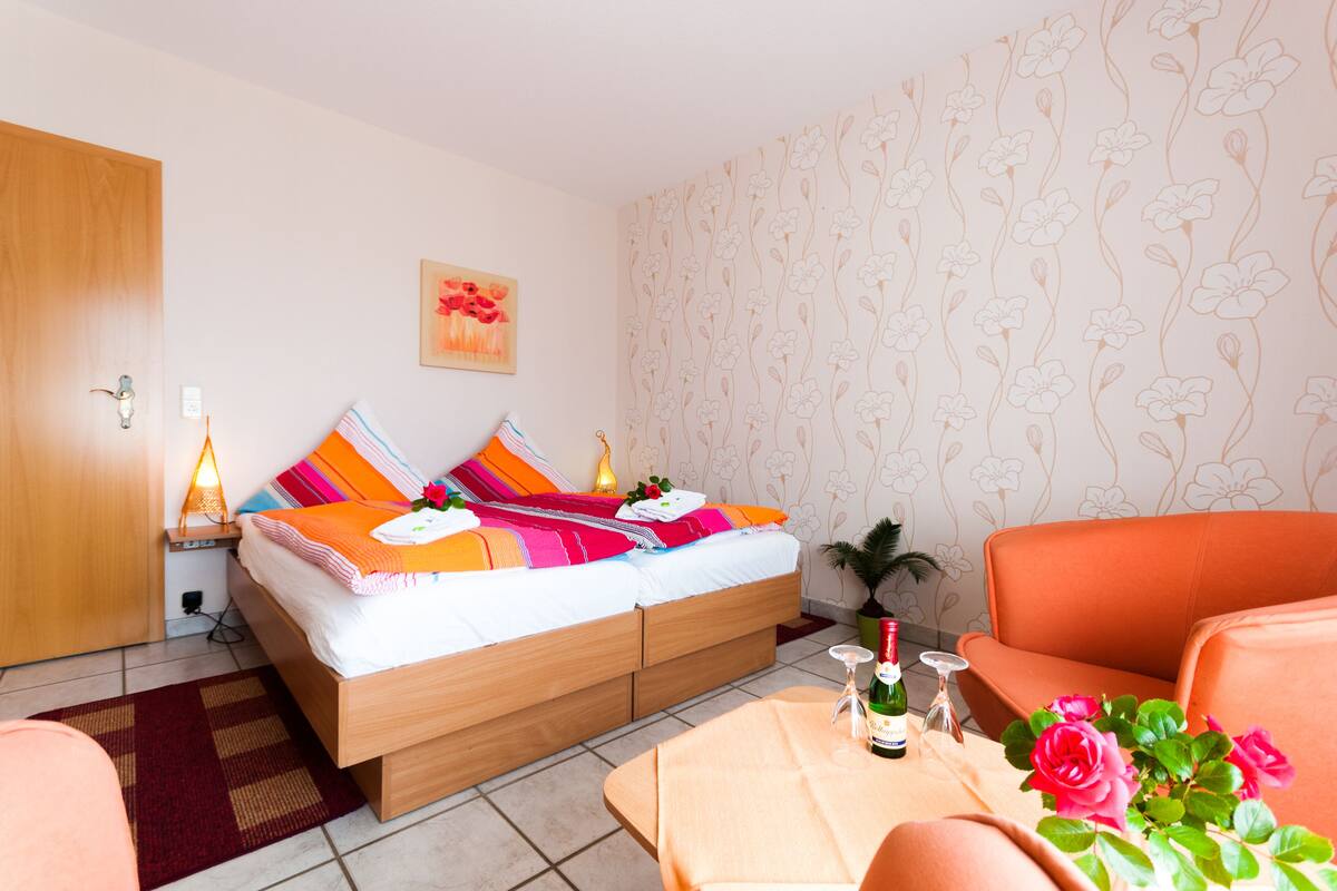 A bedroom with a bed, bedside table, lamp, and a table with a bottle and glass.