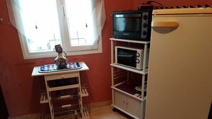 Cozinha com micro-ondas, pequena geladeira e um armário com chaleira e xícaras.