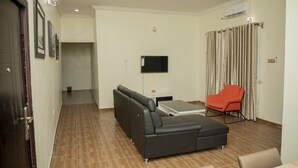 Sala de estar con sofá modular, una silla roja, televisor de pantalla plana y aire acondicionado instalado en el techo.
