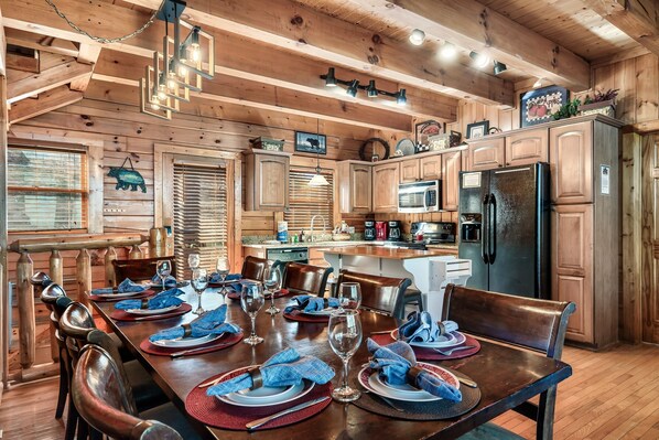 A wooden cabin interior with a dining area set for six, a kitchen with modern appliances, and a cozy ambiance.