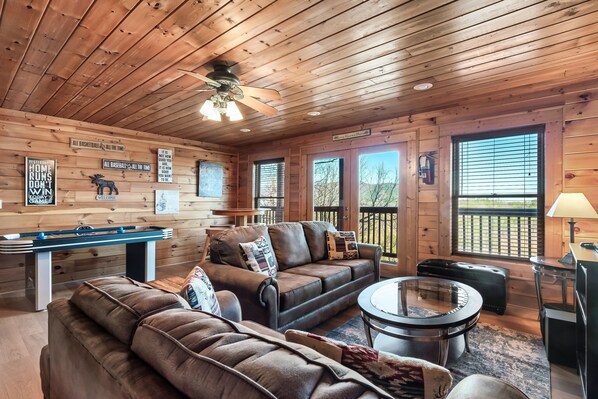 A cozy cabin interior with a pool table, leather sofas, a round coffee table, and a ceiling fan.