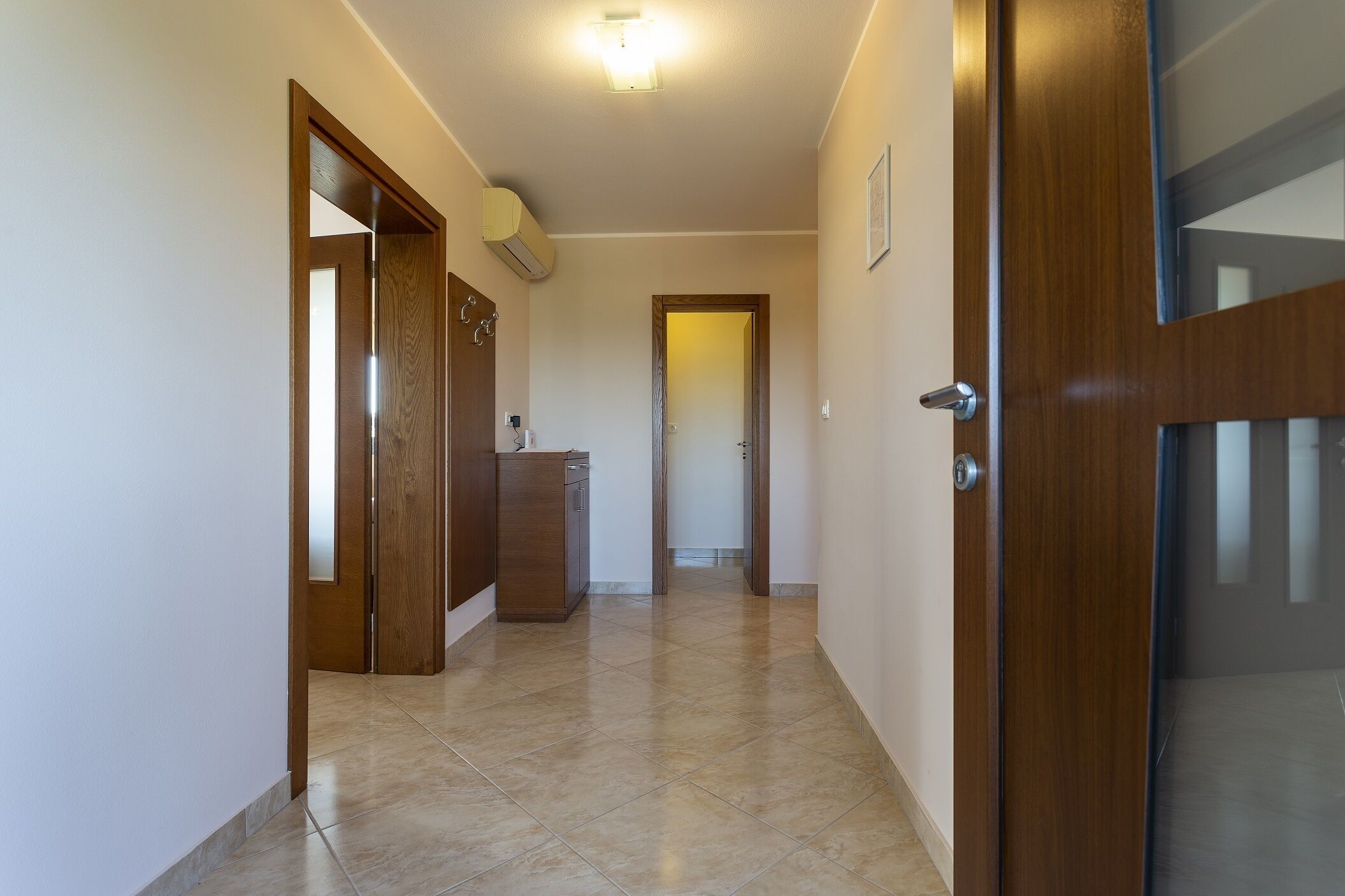 A hallway with wooden doors, a tiled floor, and a ceiling light.