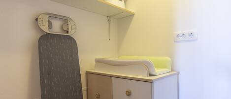 A neatly organized room with a white dresser, a shelf with a kettle and a container, and a power outlet on the wall.