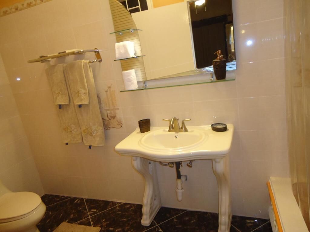 A bathroom with a white pedestal sink, a glass shelf above the sink, a towel rack with towels, and a toilet.