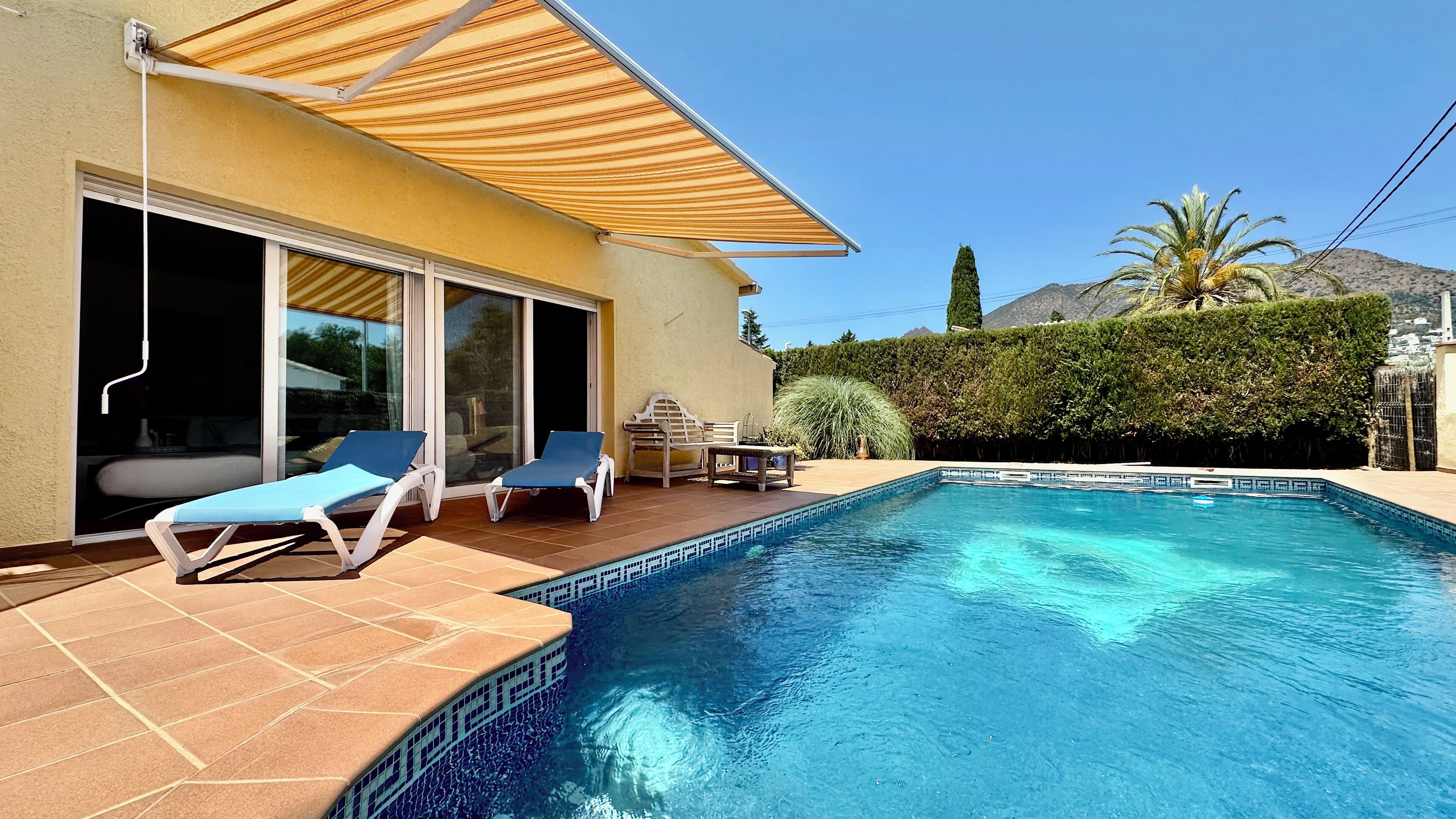 A swimming pool with lounge chairs and a patio area, surrounded by a landscaped garden and a mountain backdrop.