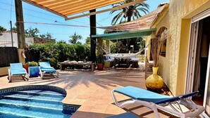 Ett poolområde med solstolar, en möblerad sittgrupp under tak och utsikt över det omgivande landskapet.