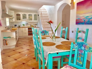 A kitchen with white cabinets, a dining table with teal chairs, and a vase with a flower.