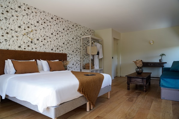 Un dormitorio ordenado con cama, mesita de noche, armario y una pequeña mesa con un florero.