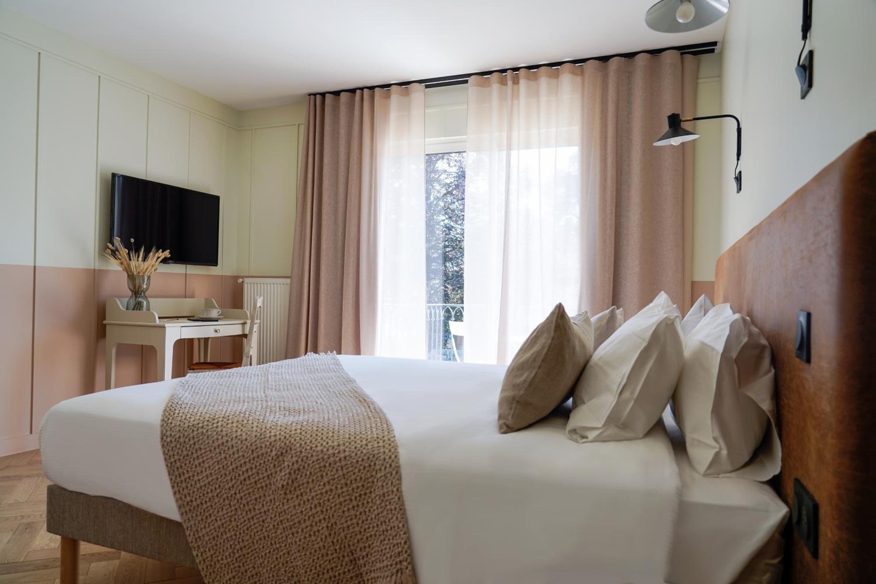 Una habitación de hotel con cama, escritorio, silla, televisor y ventana con cortinas.