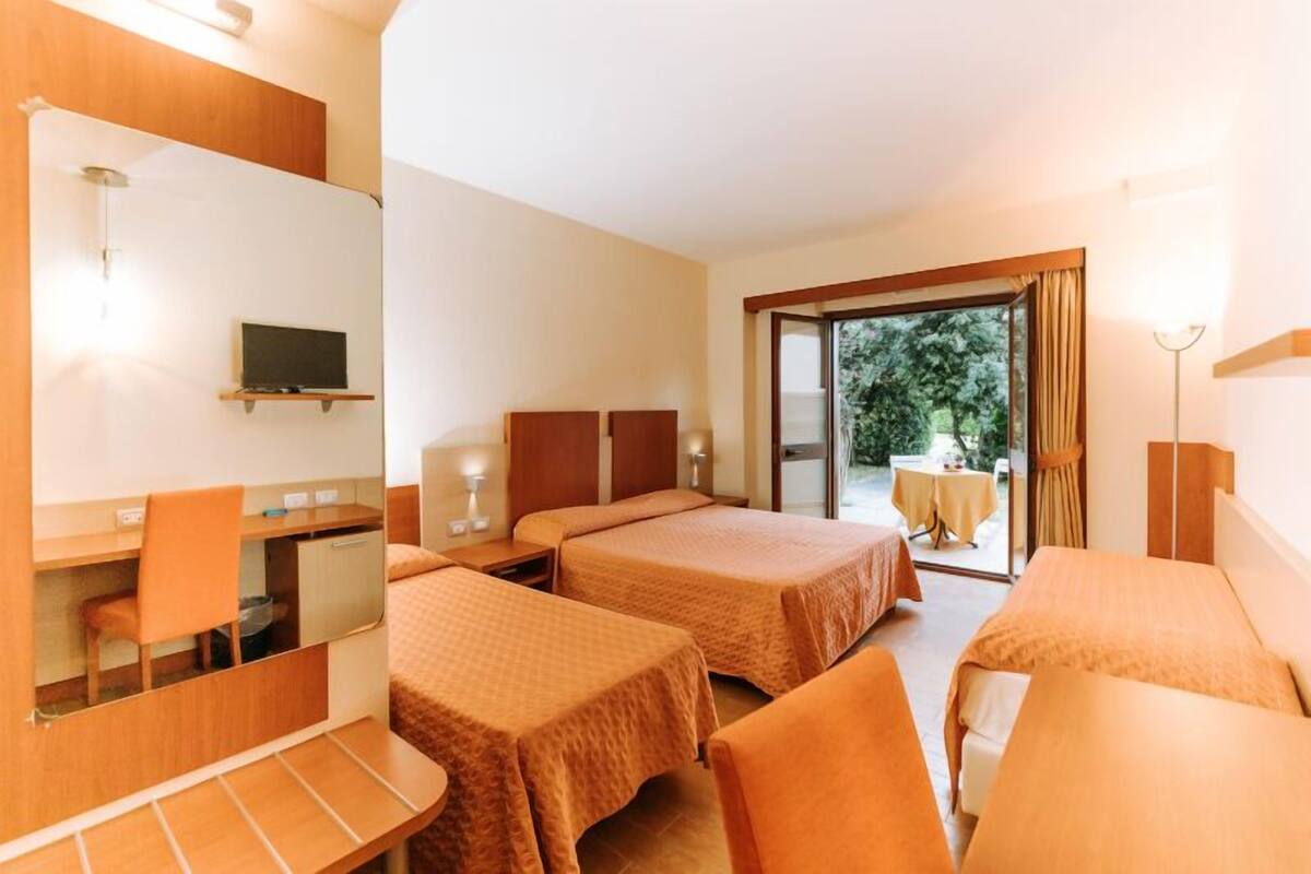 Une chambre d’hôtel avec deux lits, un bureau, une chaise, une télévision et un balcon équipé d’une table et de chaises.