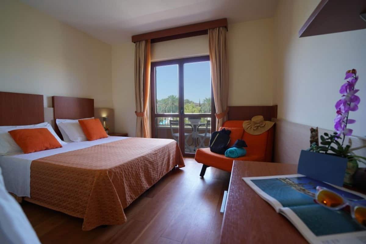 Une chambre d’hôtel avec deux lits, un balcon et une table sur laquelle se trouvent un magazine et des lunettes de soleil.