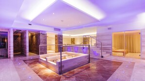 A modern spa area with a wooden bathtub, marble walls, and a staircase.