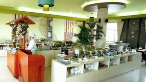 Um hall de hotel com área de recepção, serviço de buffet e uma grande planta em vaso.