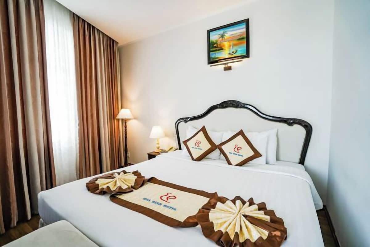 Una habitación de hotel con cama, cortinas, un cuadro y una mesita de noche con lámpara.