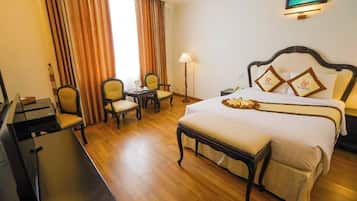 A hotel room with a bed, a desk, two chairs, a lamp, and a painting on the wall.