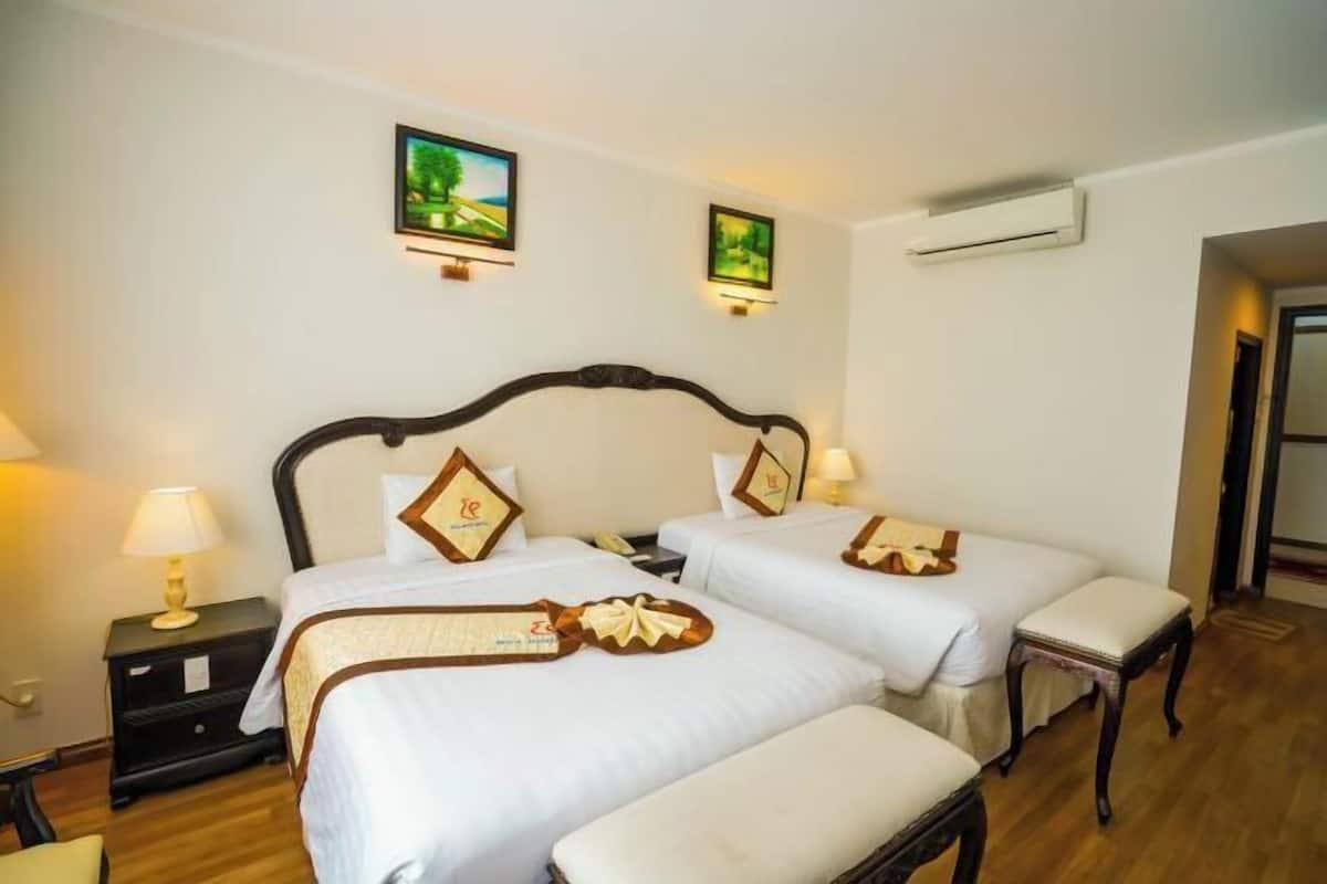 Una habitación de hotel con dos camas, una mesita de noche, una lámpara y un cuadro en la pared.