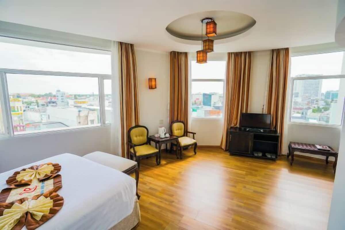 Una habitación de hotel con una cama, televisión, zona de estar con sillas, una mesita y un banco.