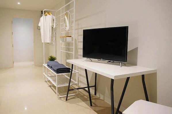 A modern room with a white desk, a flat-screen TV, a clothing rack, and a small plant. - Bed n Bev (Pattaya)