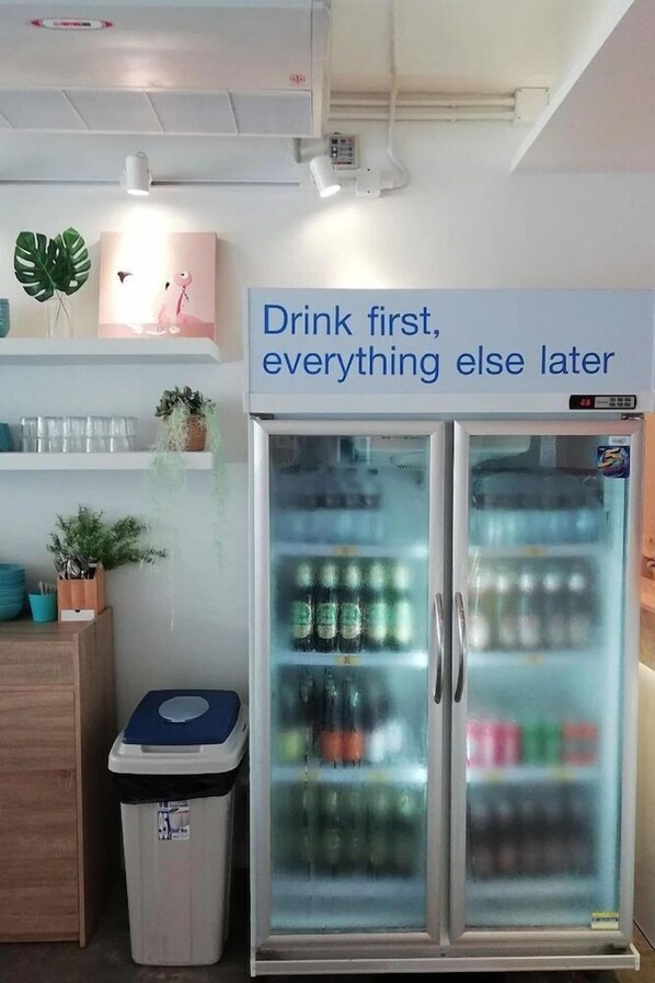 A room with a refrigerator stocked with beverages and a sign above it that reads "Drink first, everything else later." - Bed n Bev (Pattaya)