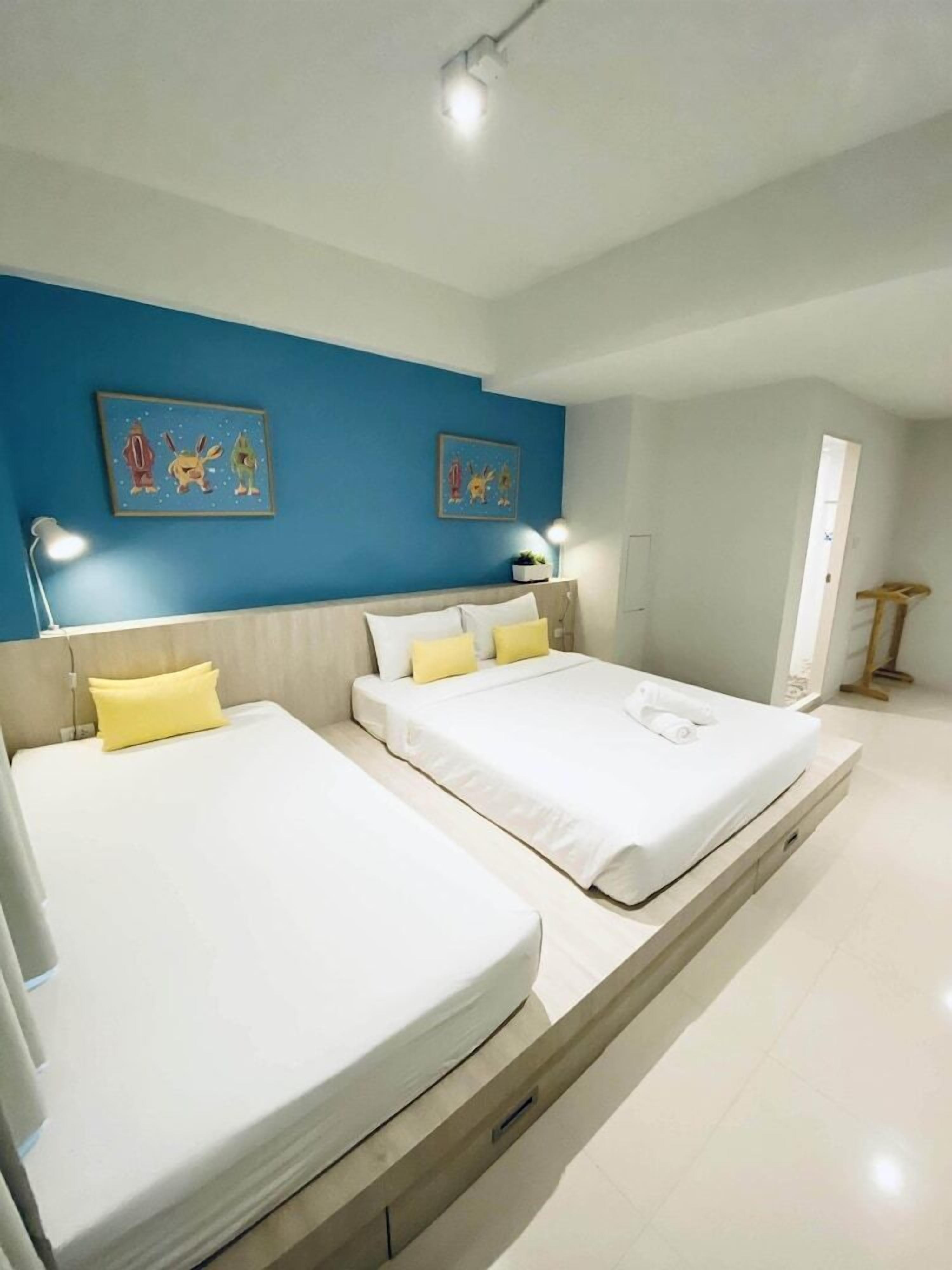 A modern bedroom with two beds, a blue accent wall, and artwork.