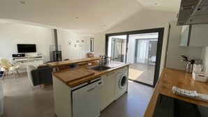 Eine moderne Küche mit Kochinsel, integriertem Geschirrspüler und Waschmaschine. Es gibt einen Essbereich mit Tisch und Stühlen sowie einen an der Wand befestigten Fernseher.