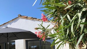 Eine Terrasss mit Korbmöbeln, einem großen Sonnenschirm und einer Glastür, die zu einem Raum führt.