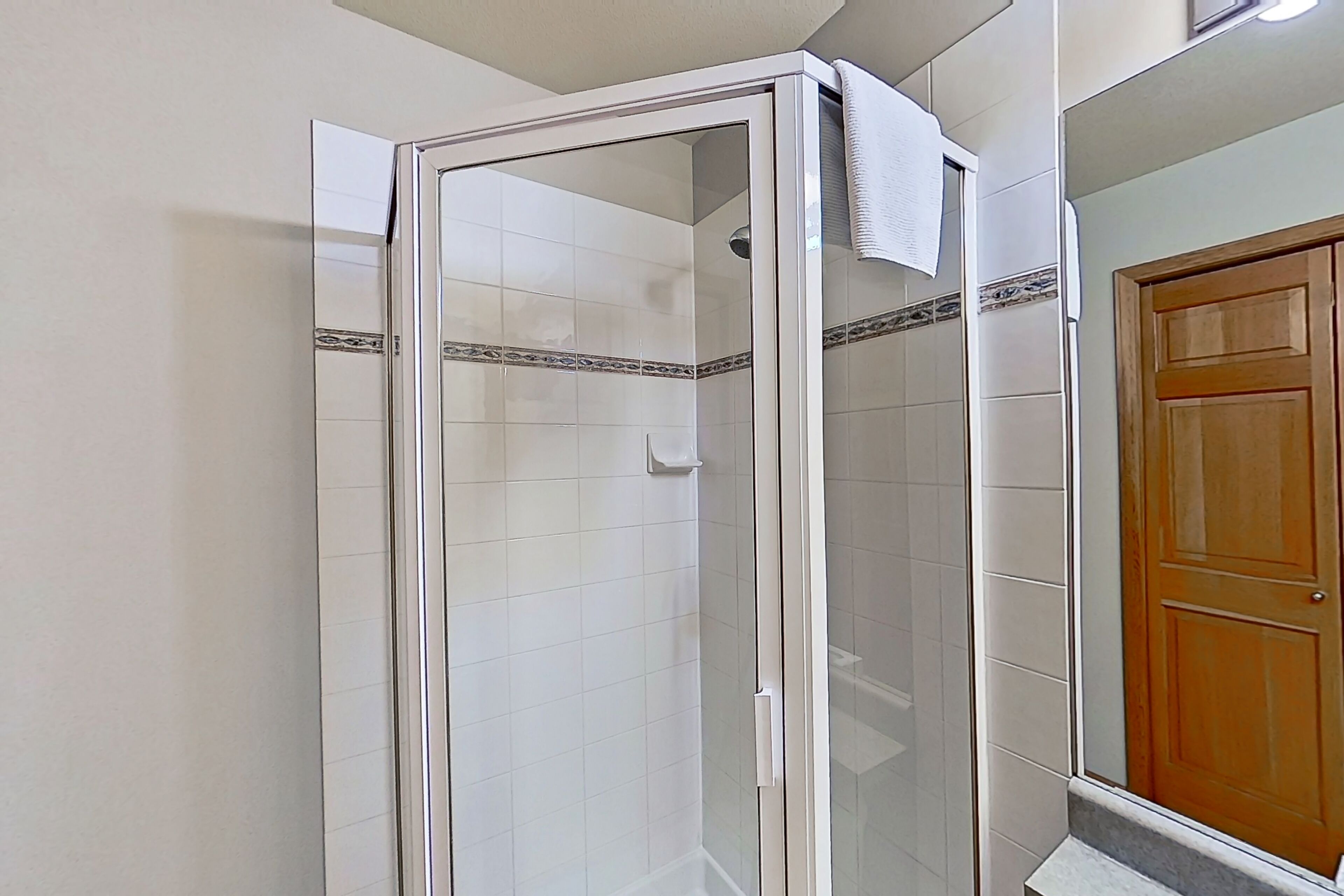 A glass-enclosed shower with white tiles and a decorative border.