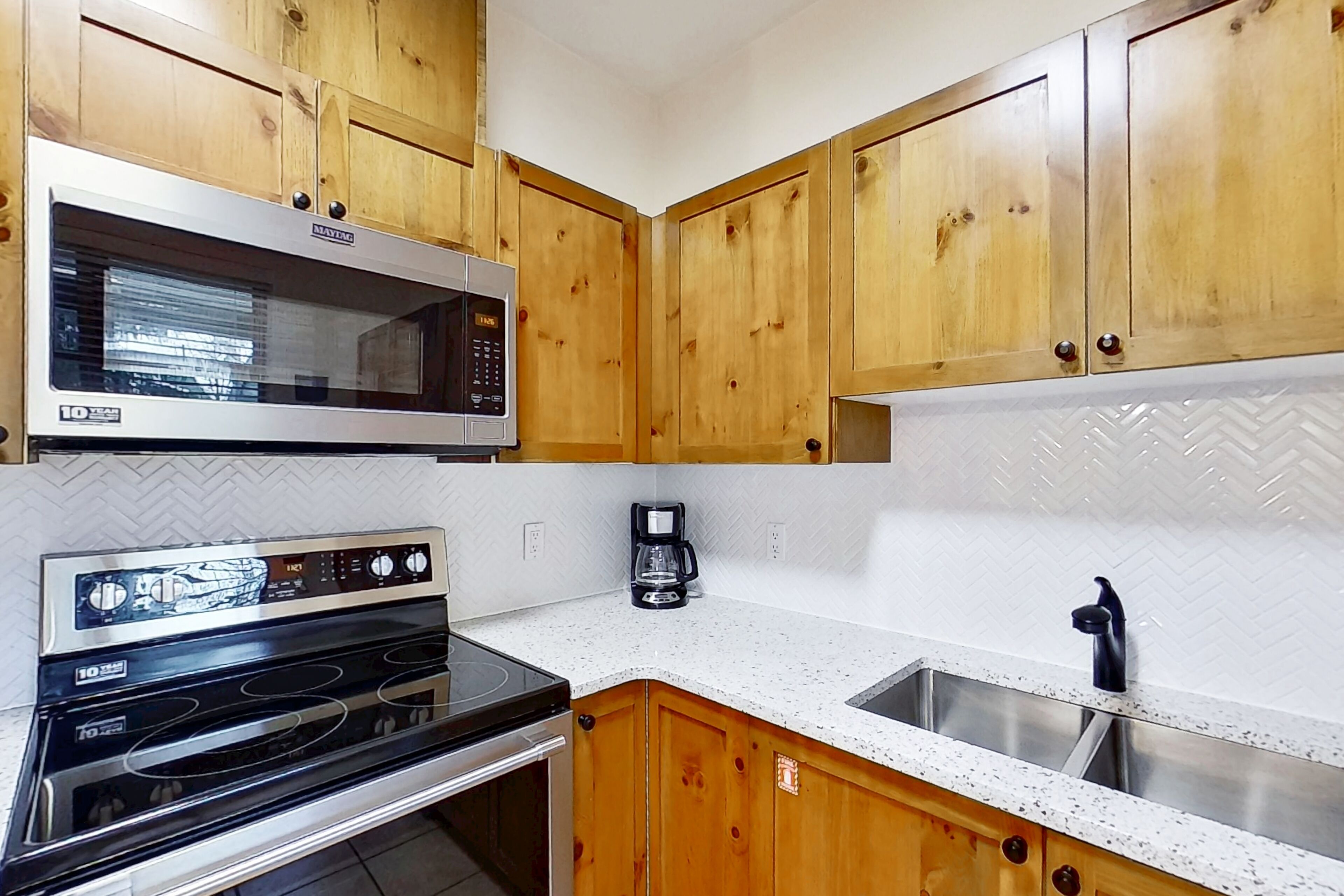 Een keuken met houten kastjes, een magnetron, een oven, een koffiezetapparaat en een spoelbak.
