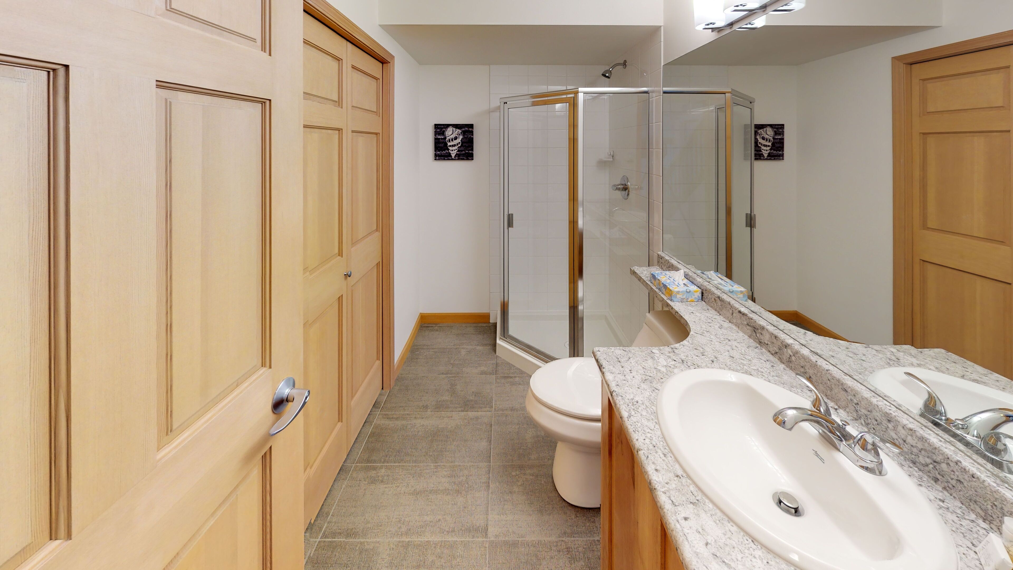 A modern bathroom with wooden cabinets, a shower, a toilet, and a large mirror.