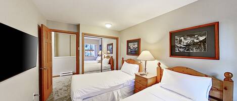 A hotel room with two beds, a TV, a mirror, and a framed picture on the wall.