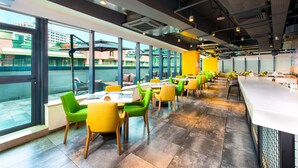 A modern dining area with large windows, green and yellow chairs, and a bar counter. - Holiday Inn Express Macau City Centre (Macau)