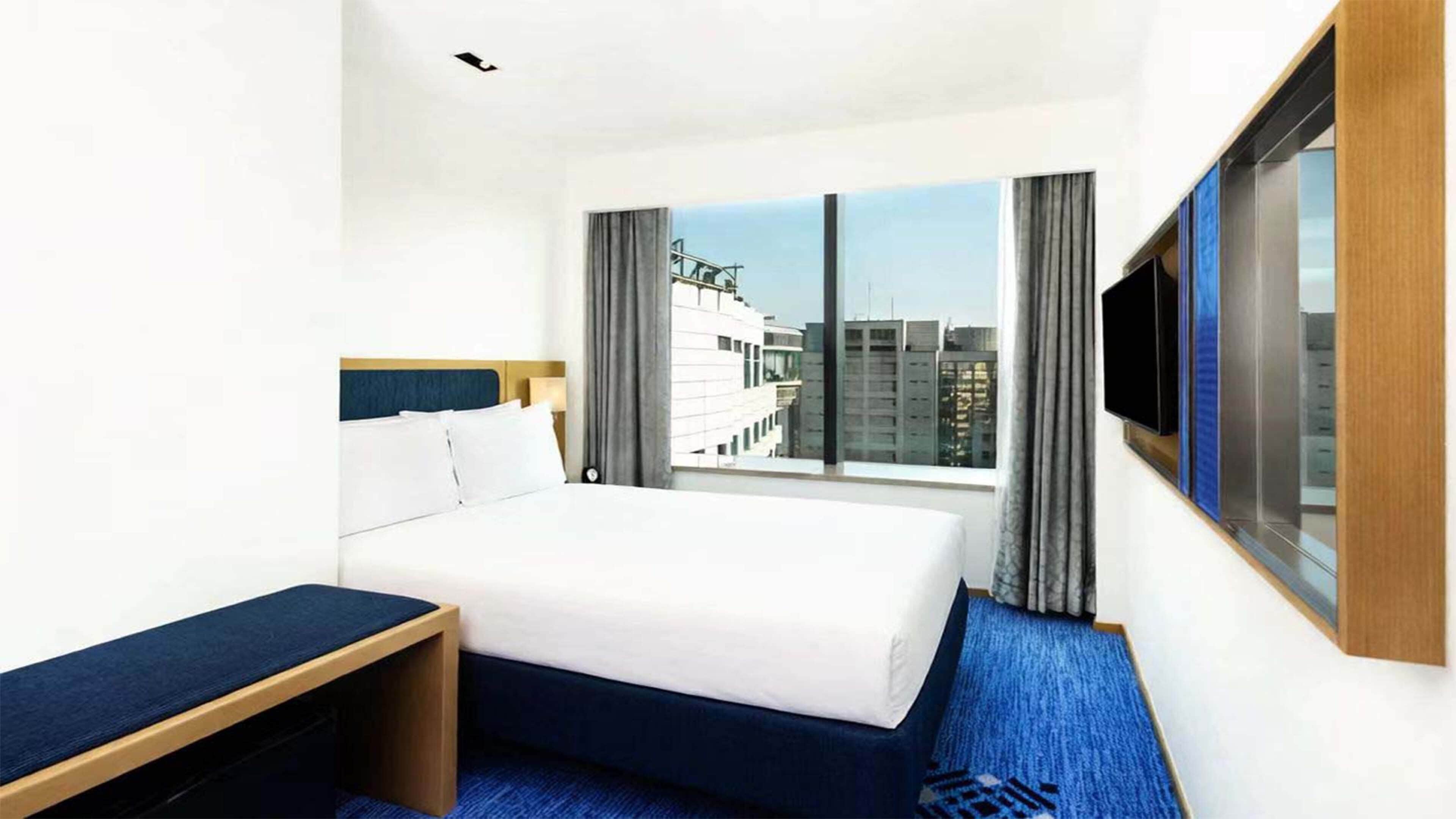 Une chambre d’hôtel avec un lit, une table de chevet, une télévision et une fenêtre donnant sur la ville.