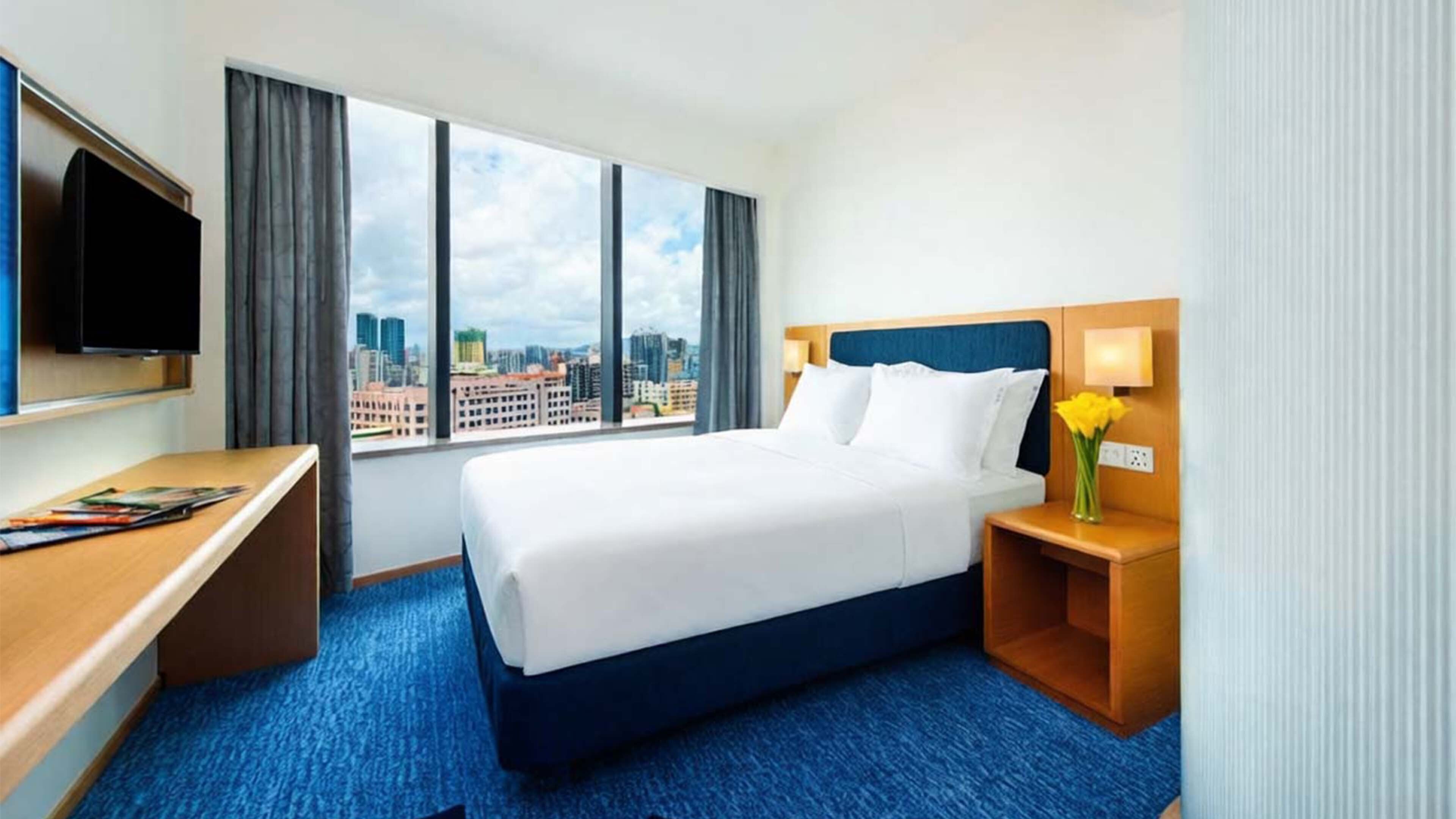 Habitación de hotel con cama, escritorio, televisión y vista a la ciudad.