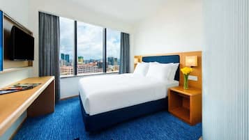 Habitación de hotel con cama, escritorio, televisión y vista a la ciudad.