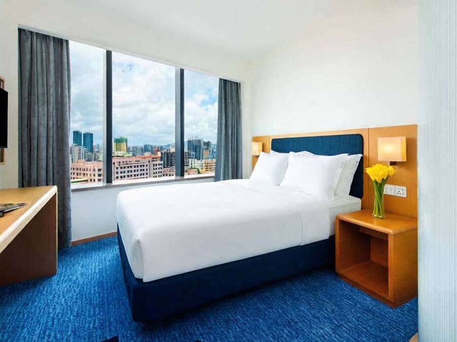 Habitación de hotel con cama, escritorio, televisión y vista a la ciudad.