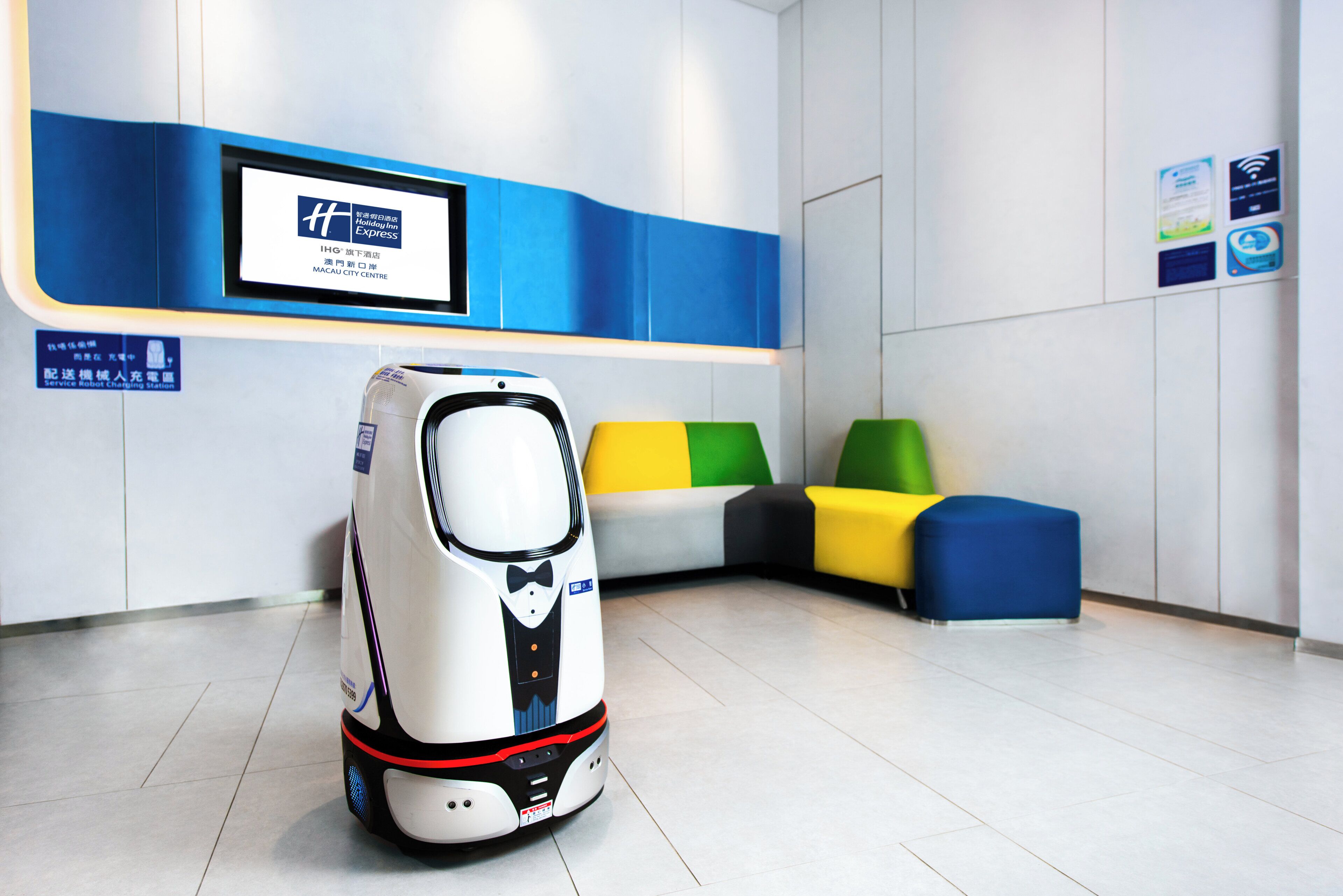 A service robot in a modern lobby with a digital display and colorful seating.