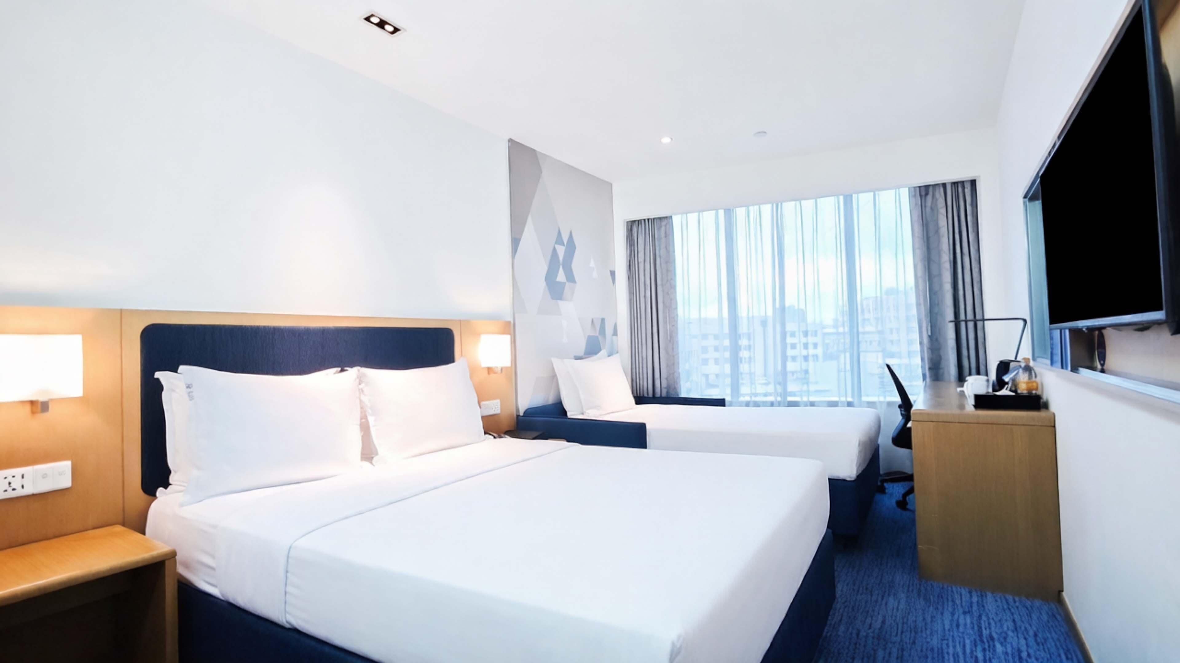Une chambre d’hôtel avec deux lits, un bureau, une télévision et une grande fenêtre donnant sur la ville.
