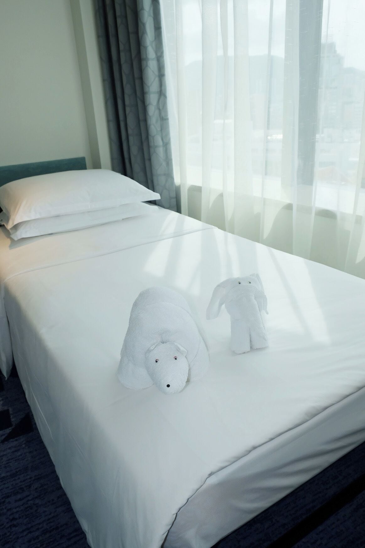 A hotel room with a neatly made bed, a pillow, and two white towels shaped like animals.