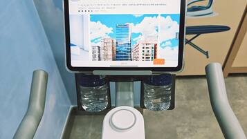 A treadmill with a digital display screen, water bottles, and a safety guard.