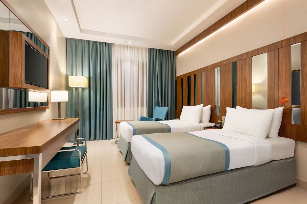 A hotel room with two beds, a desk, a chair, a TV, and a mirror.