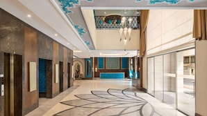 Eine Hotelhalle mit modernem Design, ausgestattet mit einer Rezeption, Aufzügen und einem dekorativen Bodenmuster.