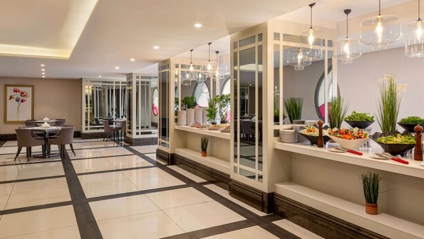 Eine moderne Hotelhalle mit Essbereich, einer Rezeption und einem Buffet mit verschiedenen Speisen und Pflanzen.