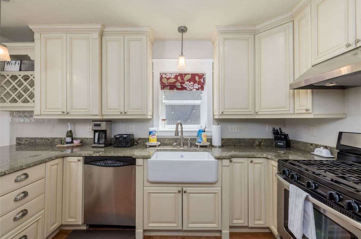 A kitchen with white cabinets, a stainless steel dishwasher, a sink, and a stove.