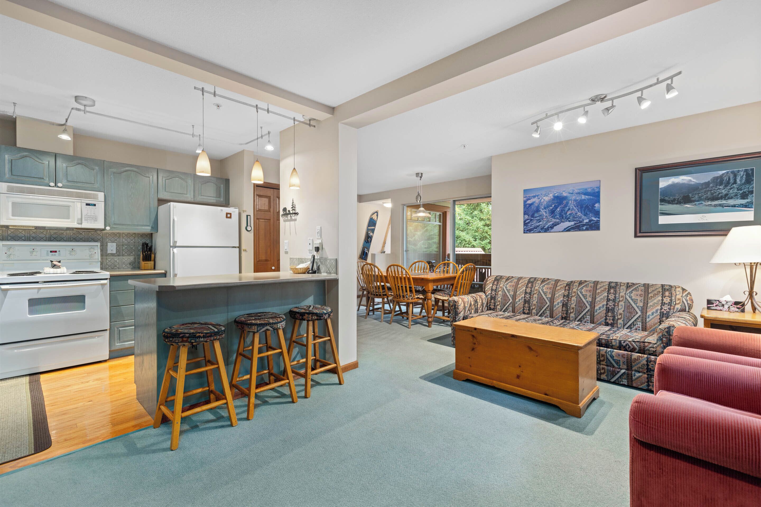 A modern kitchen with a central island, bar stools, a dining area with a table and chairs, a sofa, and a red armchair.