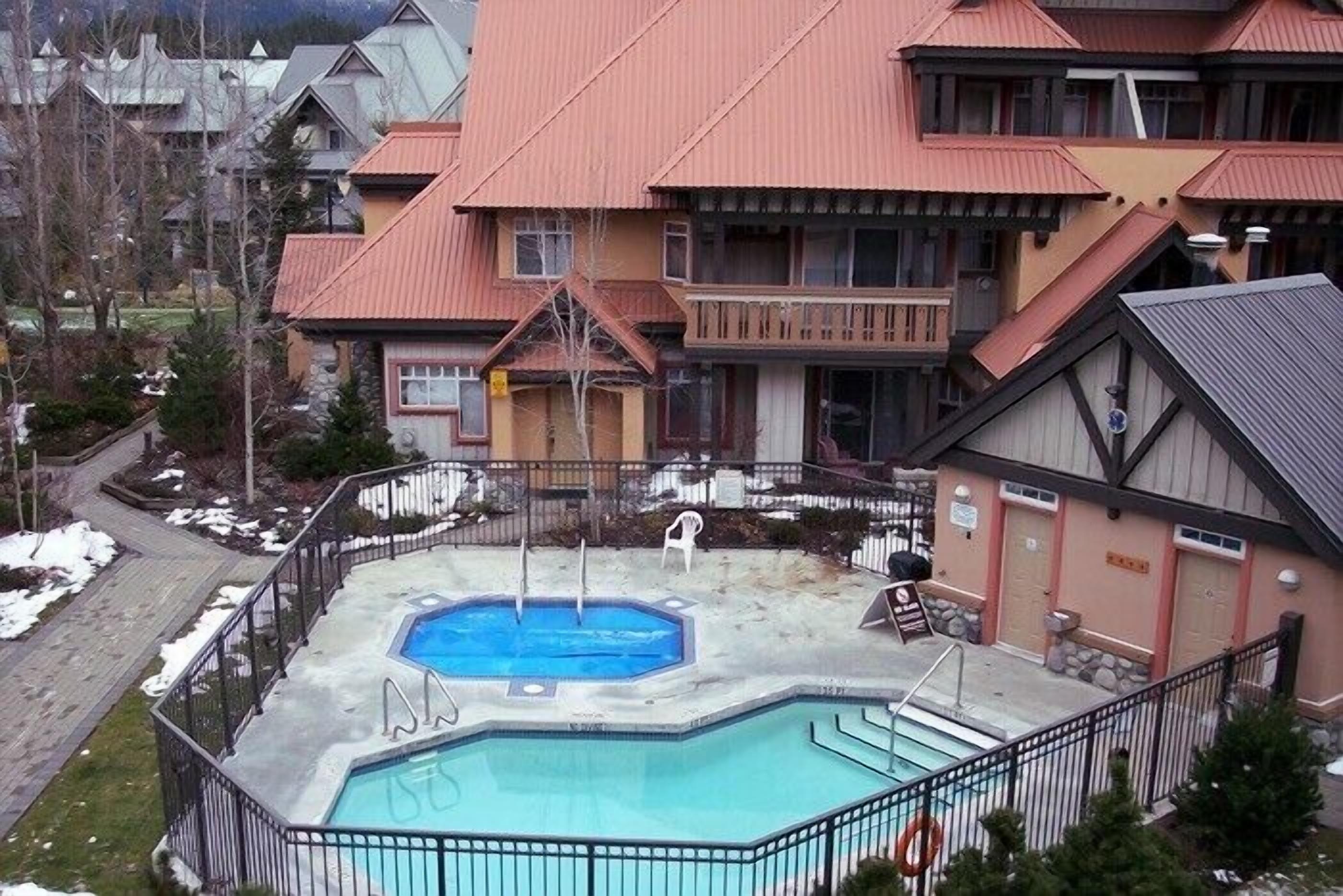 A hotel with a swimming pool, a covered deck, and a mountainous backdrop.